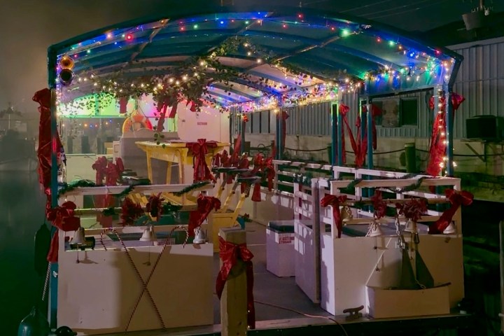 A festive boat decorated with colorful lights and red ribbons at night.